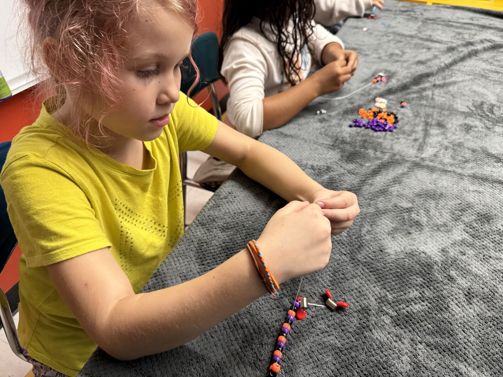 Student carefully stringing orange and purple beads onto a bracelet