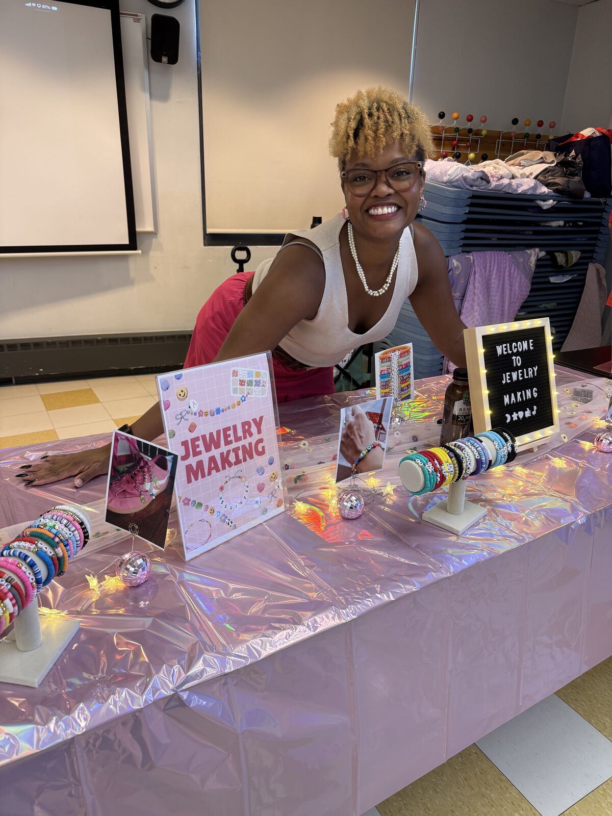 Gabriell, founder of The Innovative Learners, smiling behind a jewelry making table full of beaded bracelets