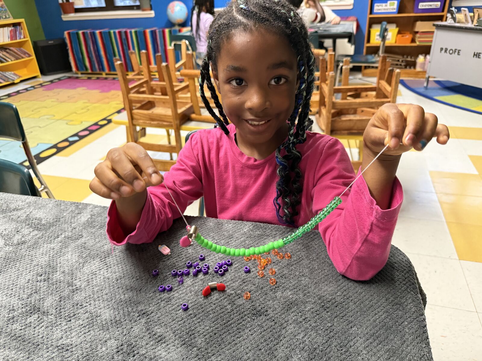Smiling student holding up a beaded necklace she designed during a jewelry design enrichment session