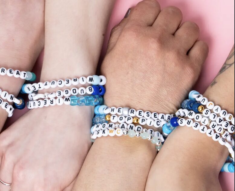Stacked beaded friendship bracelets with letter beads on several wrists